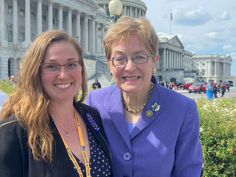 Sarah standing in business attire along with Rep. Marcy Kaptur, who is wearing a purple suit coat, the capitol building is in the background